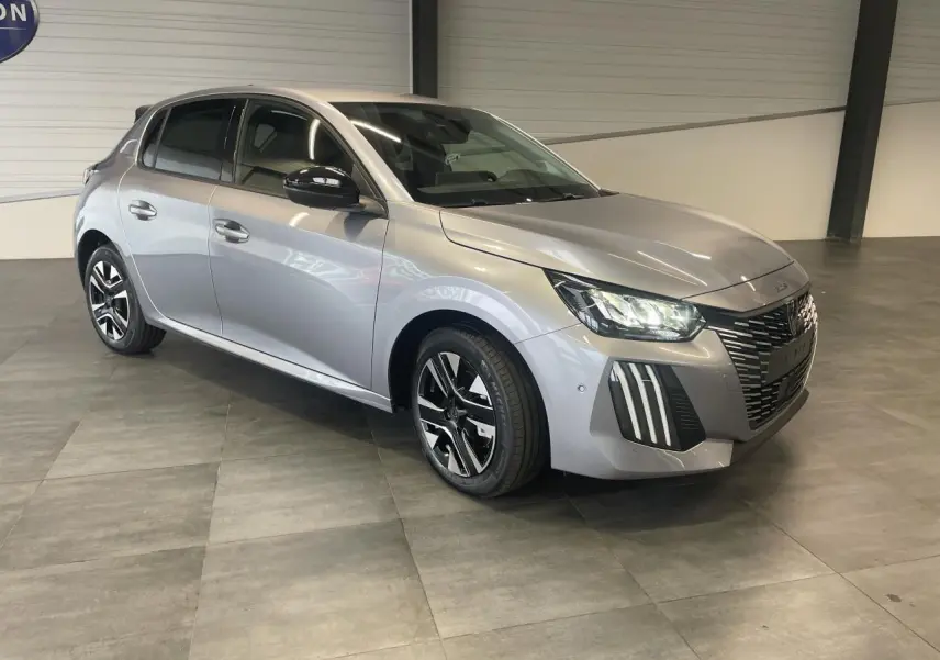 Peugeot 208 gris Artense vue 3/4 avant droit en intérieur avec jantes alliage bi-tons et calandre noire grainée.