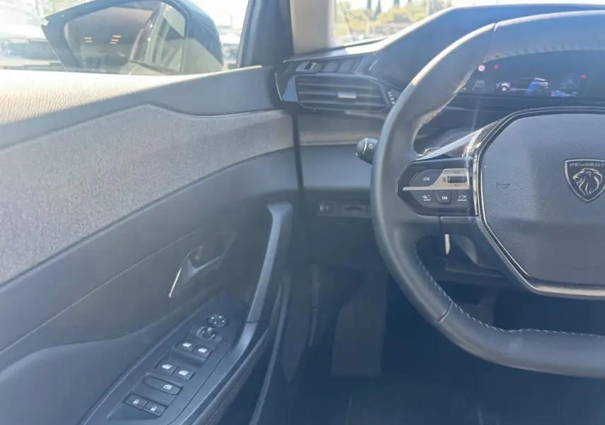Vue intérieure côté conducteur de la Peugeot 308 Hybrid gris, avec volant multifonction et commandes sur porte.