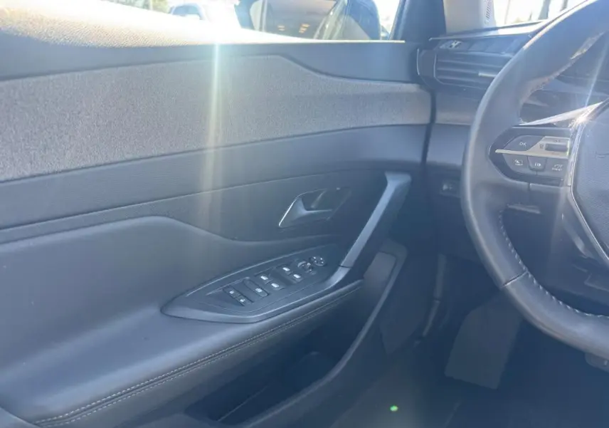 Intérieur côté conducteur de la Peugeot 308 Hybrid gris, montrant la portière avec commandes électriques et partie du volant.