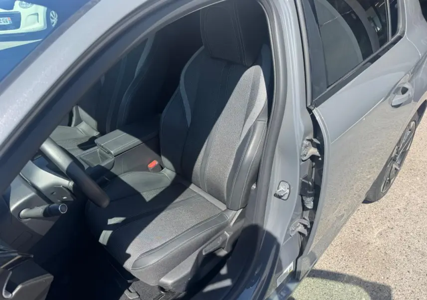 Vue intérieure côté conducteur d'une Peugeot 308 gris 2025, mettant en valeur le siège réglable en hauteur et l'accoudoir central.