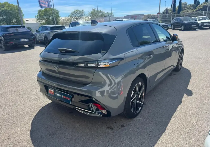 Vue 3/4 arrière droite d'une Peugeot 308 Hybrid gris métallisé avec jantes alliage 17 pouces sur parking extérieur.