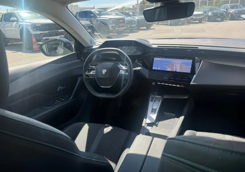 Vue intérieure avant de la Peugeot 308 Hybrid gris, mettant en valeur le volant, le cockpit numérique et l'écran tactile central.