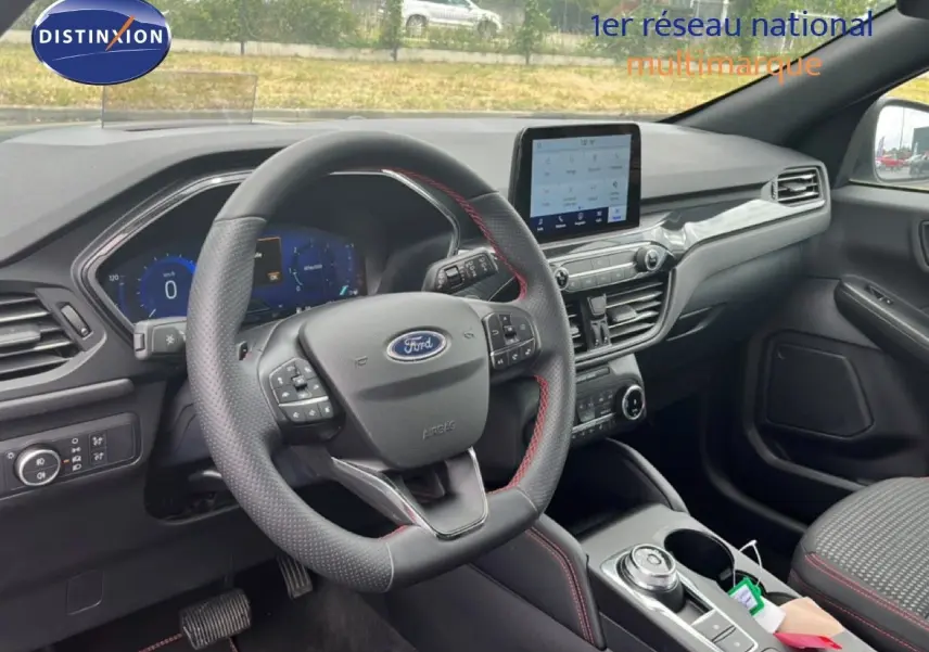 Vue intérieure côté conducteur du Ford Kuga 2024, tableau de bord moderne avec écran tactile et volant cuir noir à surpiqûres rouges.