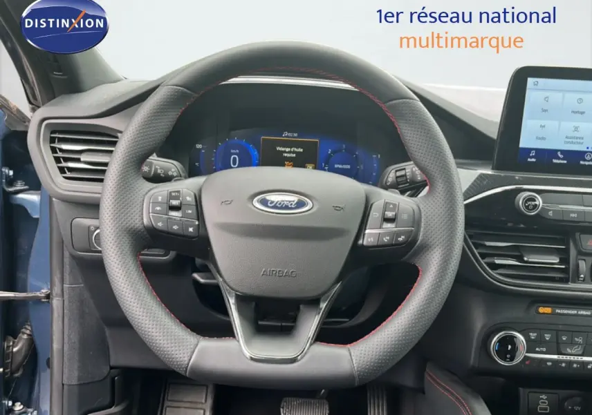 Vue rapprochée du volant cuir noir avec surpiqûres rouges et tableau de bord numérique du Ford Kuga bleu chrome 2024.