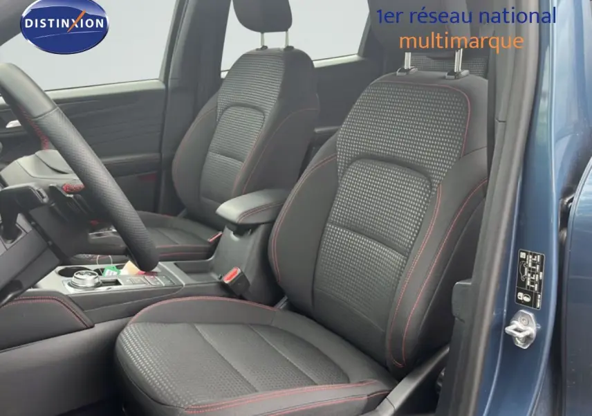 Vue intérieure côté conducteur du Ford Kuga 2024 bleu chrome, sièges tissu noir avec surpiqûres rouges et volant multifonction.