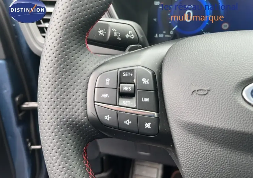 Gros plan sur le volant perforé avec surpiqûres rouges du Ford Kuga bleu chrome, montrant les commandes multifonctions à gauche.