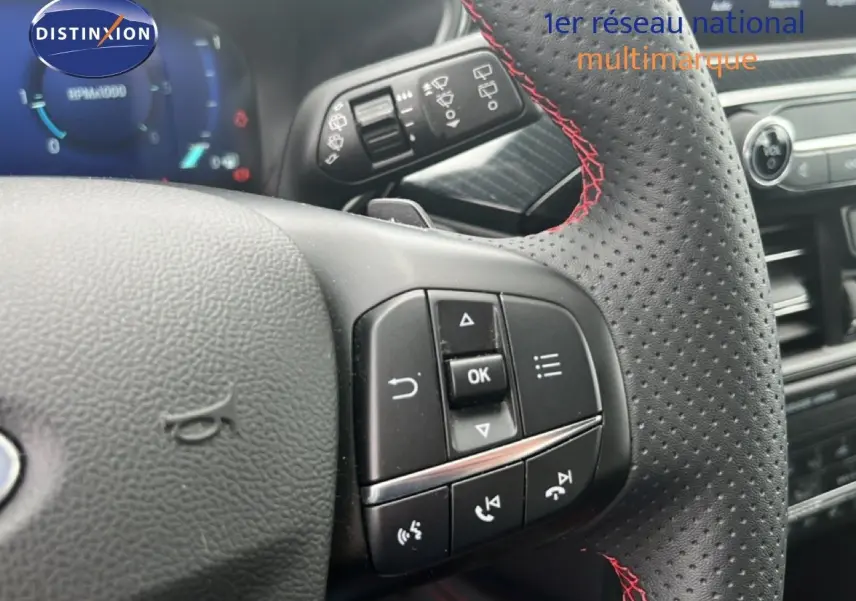 Gros plan sur le volant perforé avec surpiqûres rouges du Ford Kuga 2024, montrant les commandes multifonctions.