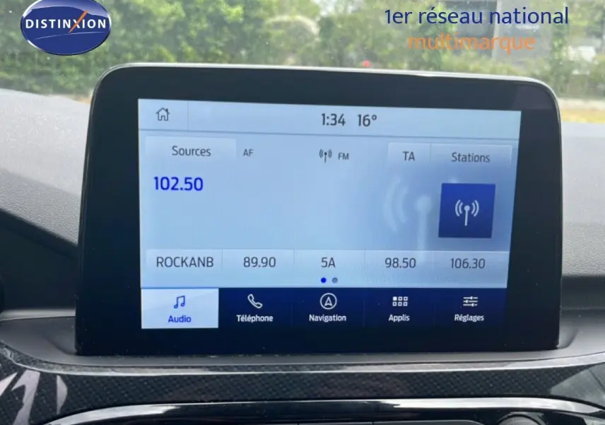 Écran tactile central du Ford Kuga 2024 affichant la radio FM, avec tableau de bord en finition noire.