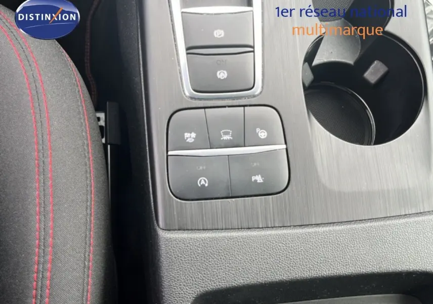 Gros plan sur la console centrale du Ford Kuga 2024 bleu chrome, avec boutons de contrôle et porte-gobelet visible.