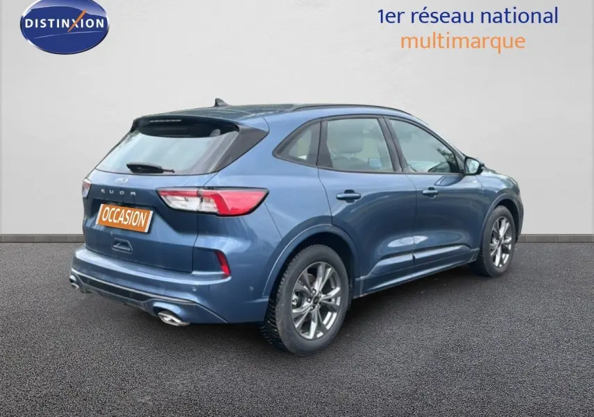 Ford Kuga 2024 bleu chrome métal en vue 3/4 arrière droit, finition ST-LINE avec jantes alliage et double sortie d’échappement.