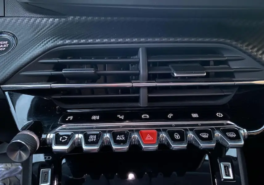 Gros plan sur la console centrale noire brillante du Peugeot 2008 avec commandes climatisation et bouton rouge d'alerte