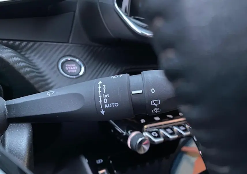 Gros plan sur la commande d'essuie-glace à gauche du volant dans l'habitacle noir d'une Peugeot 2008 blanche de 2020.