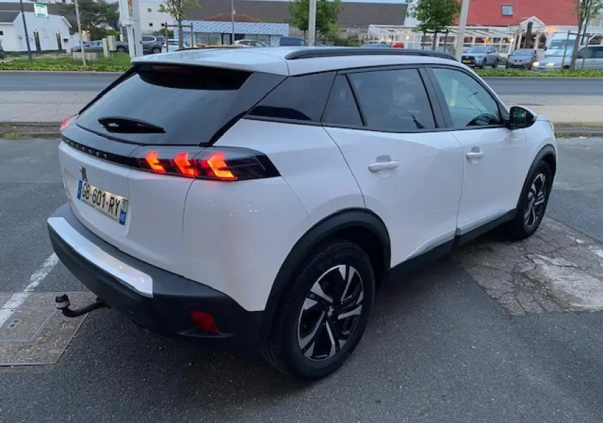 Peugeot 2008 blanc vue 3/4 arrière droit avec jantes bi-tons et attelage col de cygne visible.