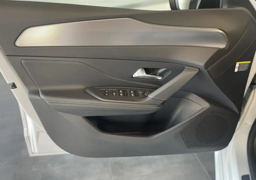 Porte avant gauche ouverte d'une Peugeot 308 blanche 2025, garniture noire avec surpiqûres vertes et insert aluminium.