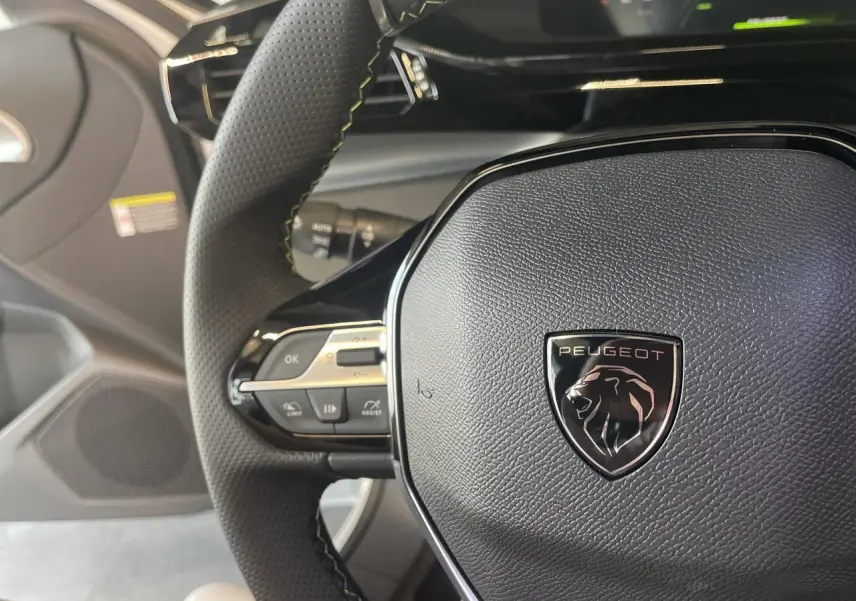 Gros plan sur le volant cuir noir de la Peugeot 308 2025 avec logo lion et commandes intégrées côté gauche.