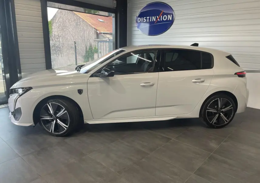 Peugeot 308 blanche vue de profil côté gauche en intérieur, avec jantes alliage noires et vitres teintées.