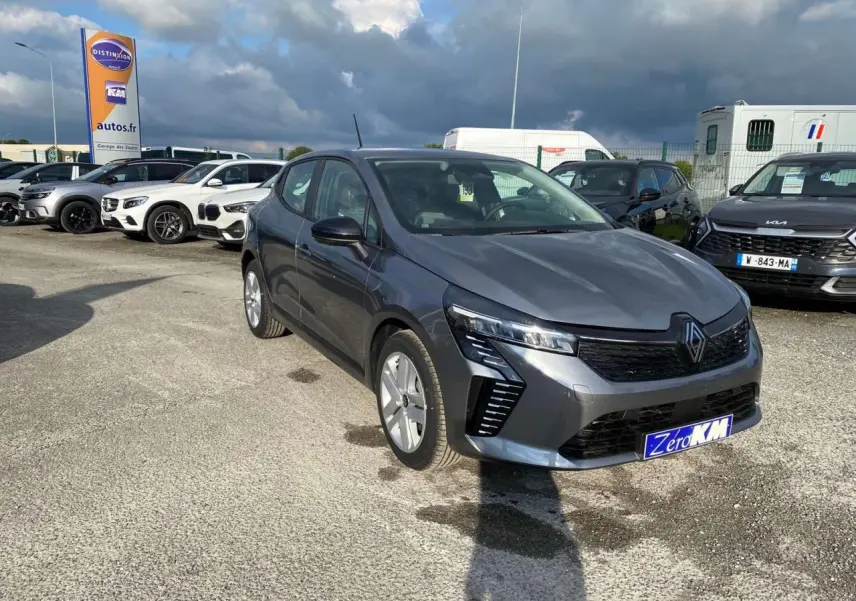 Renault Clio 2025 gris schiste vue 3/4 avant avec phares LED et calandre noire sur parking extérieur.