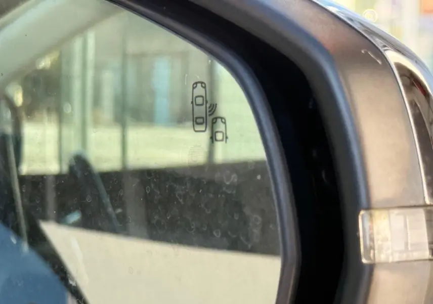 Gros plan sur le rétroviseur droit d'un Peugeot 3008 blanc nacré avec icône d'alerte d'angle mort visible.