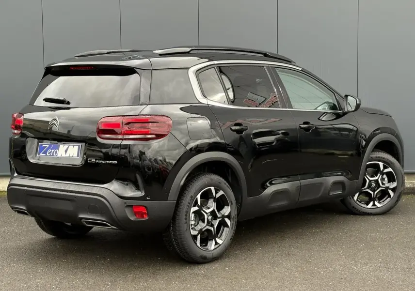 Vue 3/4 arrière droite d'un Citroën C5 Aircross noir Perla avec jantes alliage bi-ton et barres de toit noires.
