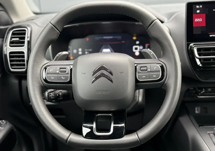 Vue rapprochée du volant cuir noir avec commandes intégrées du Citroën C5 Aircross Hybrid 2025, tableau de bord et écran tactile visibles.