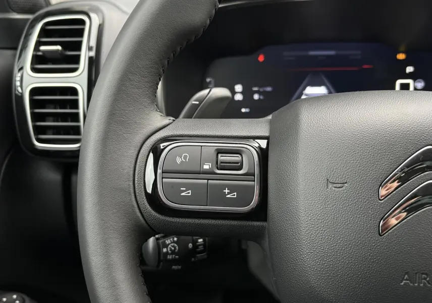 Gros plan sur le volant noir cuir de la Citroën C5 Aircross Hybrid 2025, avec commandes intégrées et logo chromé.