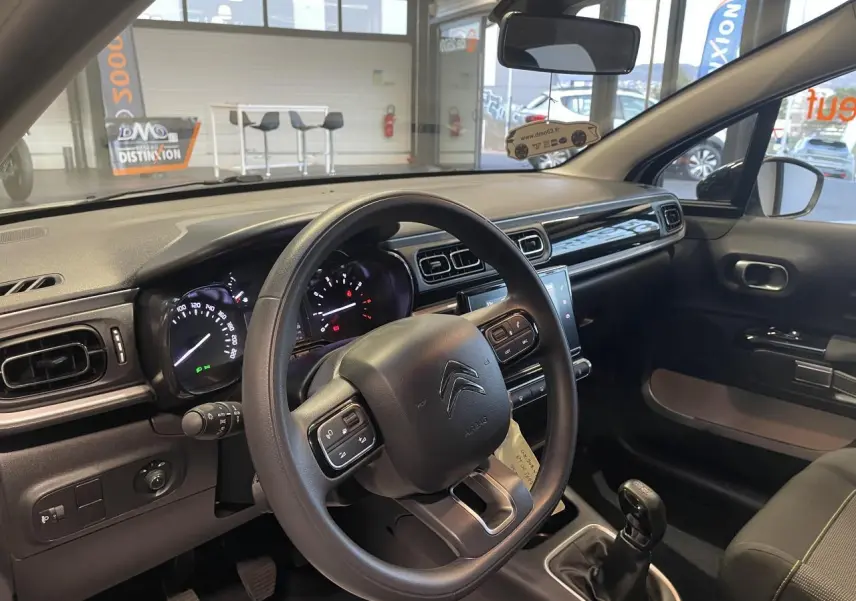 Vue intérieure côté conducteur du tableau de bord et volant noir de la Citroën C3 beige clair 2024 avec boîte manuelle.