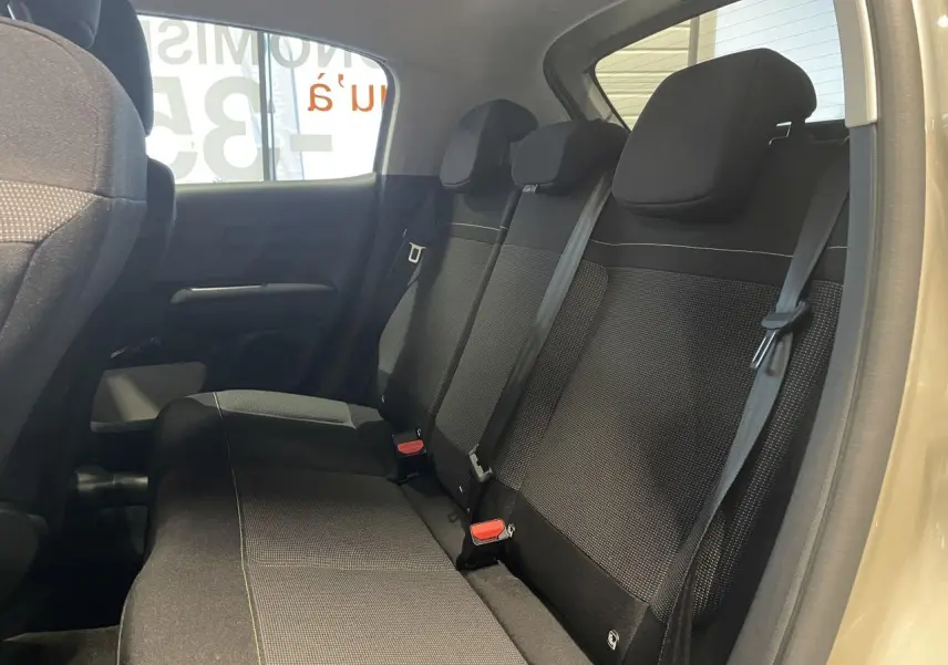 Vue intérieure côté droit montrant la banquette arrière noire avec ceintures de sécurité sur Citroën C3 beige clair 2024.