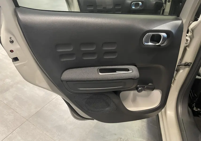 Vue intérieure côté gauche de la porte arrière beige clair d'une Citroën C3 2024 avec poignée chromée et manivelle de vitre.