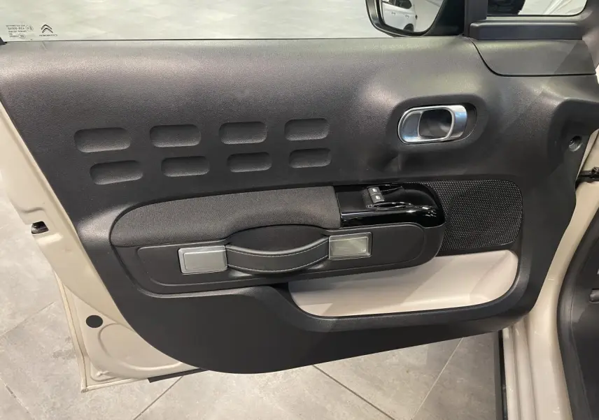 Vue intérieure côté gauche de la porte noire et beige clair d'une Citroën C3 2024 avec poignée et commandes de vitres.