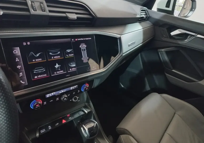Vue intérieure côté passager de l'Audi Q3 blanc, mettant en valeur l'écran tactile central et la console moderne.