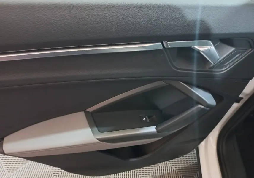 Intérieur de la porte avant droite de l'Audi Q3 blanc, avec poignée argentée et commande de vitre noire.
