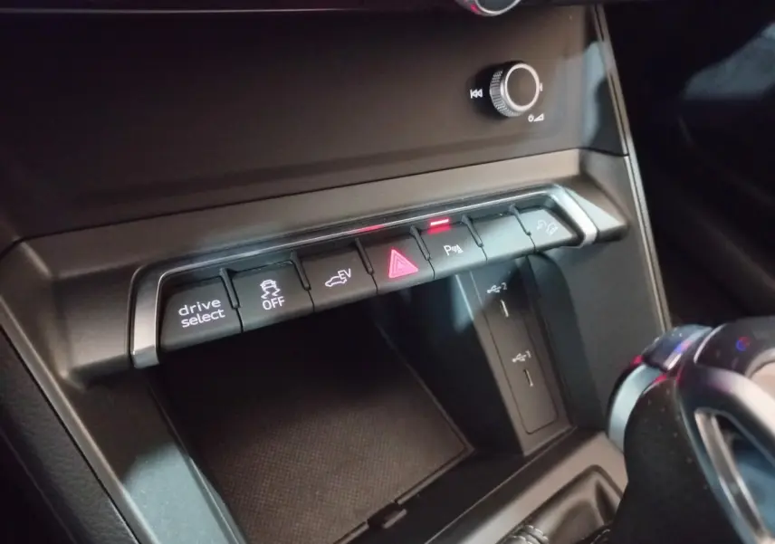 Gros plan sur la console centrale noire de l'Audi Q3 45 TFSI e 2021, montrant les boutons de contrôle et ports USB.