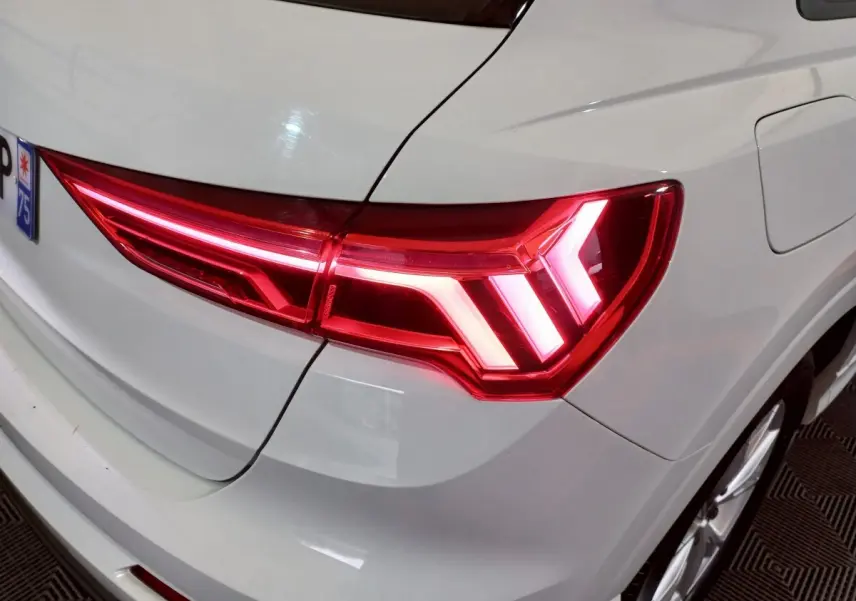 Feu arrière droit allumé d’un Audi Q3 blanc, vue rapprochée sur la partie arrière droite du véhicule.