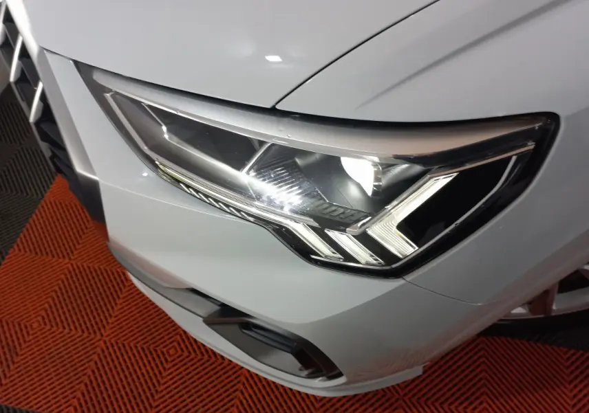 Gros plan sur le phare avant droit blanc d’un Audi Q3 45 TFSI e S line 2021, avec éclairage LED distinctif.