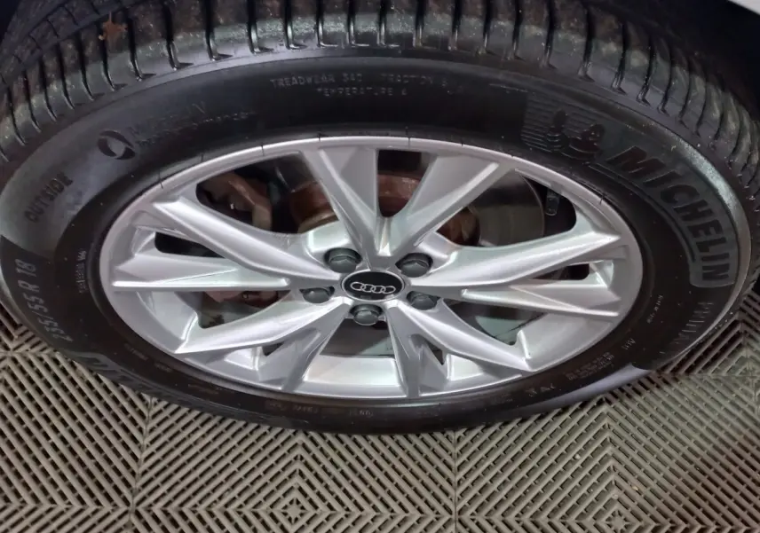 Gros plan sur la jante alliage argentée avec logo Audi au centre, montée sur pneu Michelin, véhicule blanc hybride Audi Q3.