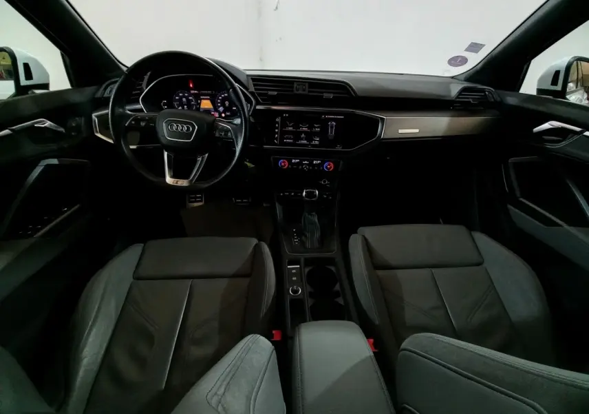 Vue intérieure avant de l'Audi Q3 blanc 45 TFSI E 245 S tronic S line, avec tableau de bord numérique et volant cuir multifonctions.