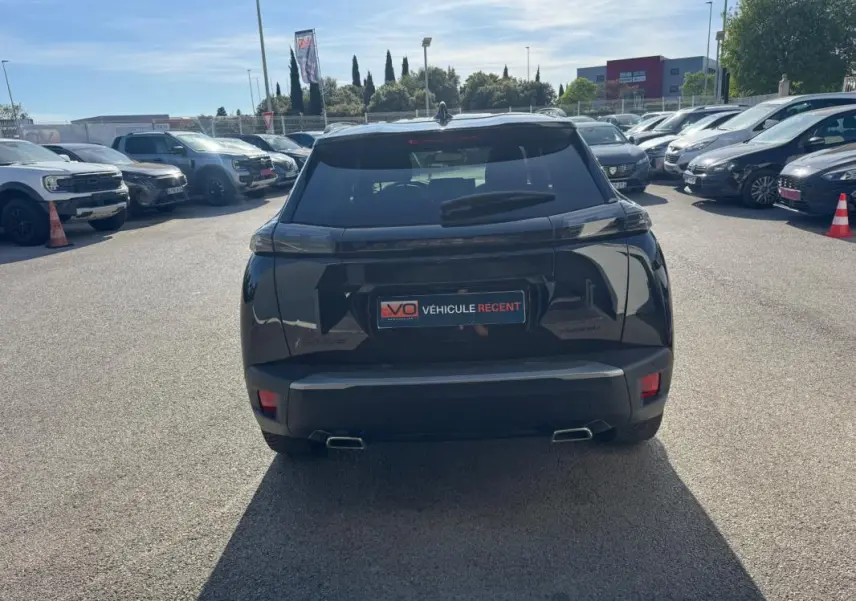 Vue arrière d'un Peugeot 2008 Hybrid noir 2025 avec barres de toit et jantes alliage 17 pouces, stationné en extérieur.
