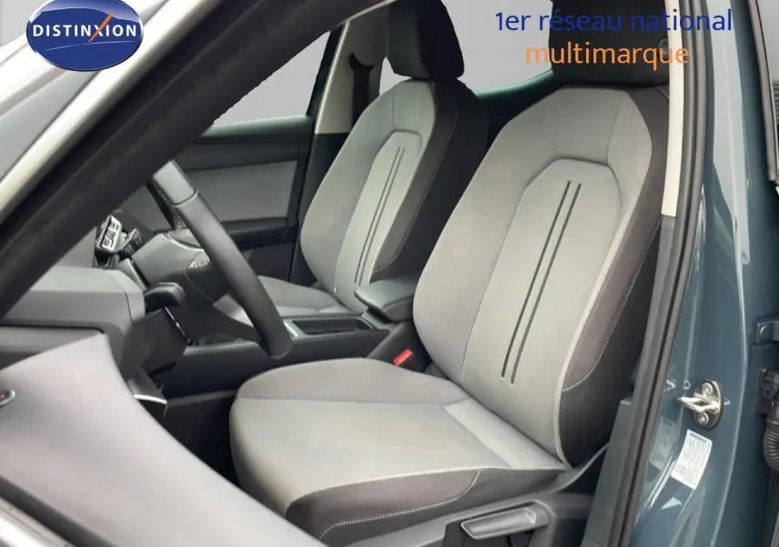 Vue intérieure côté conducteur d’une SEAT LEON gris magnétique métal, mettant en valeur les sièges tissu gris clair et foncé.