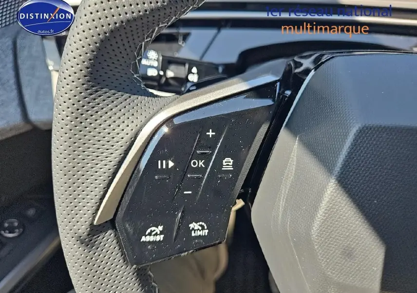 Gros plan sur les commandes gauche du volant cuir perforé du Peugeot 5008 Hybrid 145 gris titane.