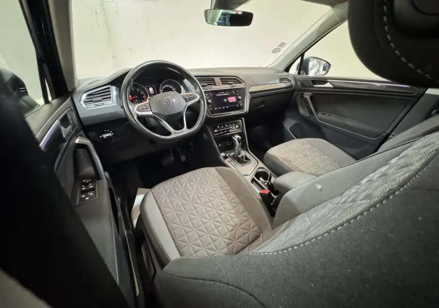 Vue intérieure avant du Volkswagen Tiguan 2021, sièges gris à motifs, volant cuir multifonctions et écran tactile central.