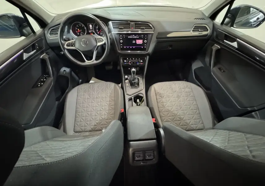 Vue intérieure avant du Volkswagen Tiguan 1.5 TSI 2021, montrant tableau de bord, volant multifonctions et sièges gris à motifs.