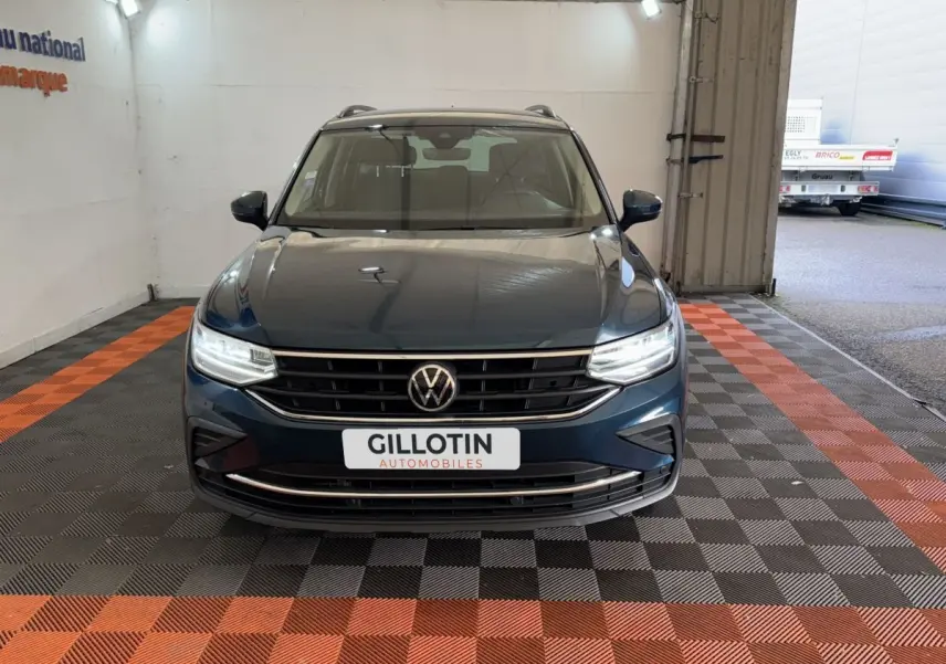 Vue frontale d'un Volkswagen Tiguan bleu avec phares LED allumés et rails de toit noirs en intérieur.