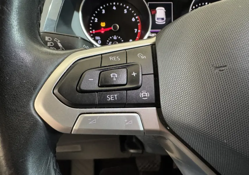 Gros plan sur les commandes multifonctions du volant cuir du Volkswagen Tiguan 1.5 TSI bleu, avec tableau de bord partiellement visible.