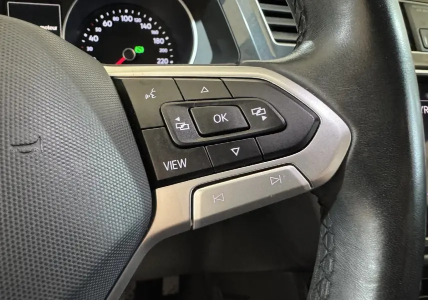 Gros plan sur les commandes multifonctions à droite du volant cuir noir du Volkswagen Tiguan bleu, tableau de bord en arrière-plan.