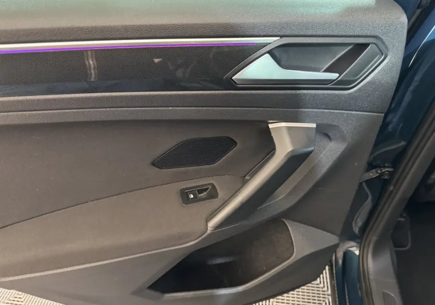 Détail de la porte arrière gauche du Volkswagen Tiguan bleu, avec éclairage d’ambiance violet et poignée argentée.