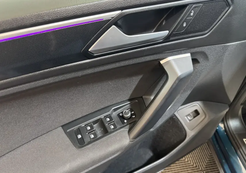Vue intérieure côté conducteur de la portière du Volkswagen Tiguan bleu, avec commandes de vitres et verrouillage.