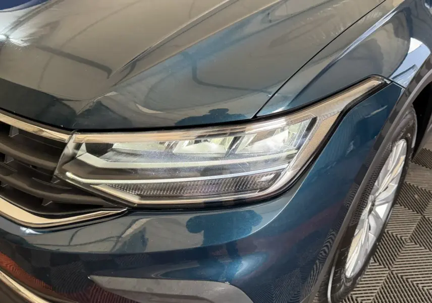 Gros plan sur l'avant droit bleu métallisé du Volkswagen Tiguan 2021, mettant en valeur le phare LED et la calandre.