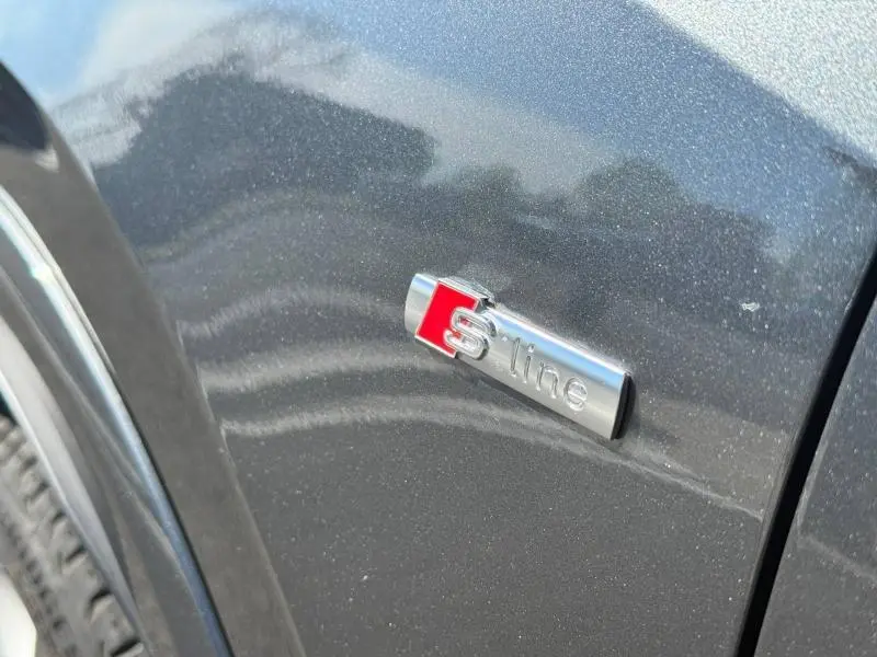 Gros plan sur l'emblème S line sur la carrosserie gris Daytona nacré d'un Audi Q2 35 TDI 2025.