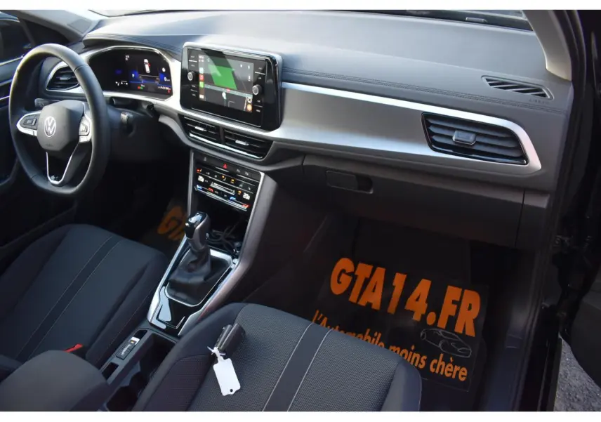 Vue intérieure côté passager du Volkswagen T-Roc 2025, montrant la console centrale, volant et sellerie tissu noir.