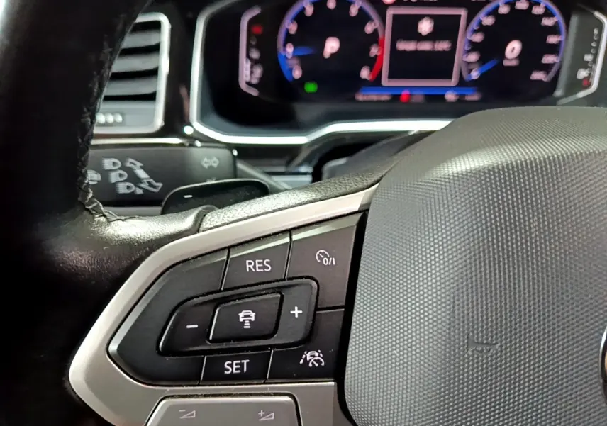 Gros plan sur le volant multifonctions en cuir et alu du Volkswagen Taigo blanc, avec tableau de bord numérique en arrière-plan flou.